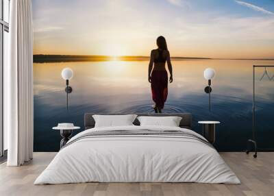 Silhouette woman on the beach at sunset . She stands in water. Morning natural stretch warm-up training Wall mural