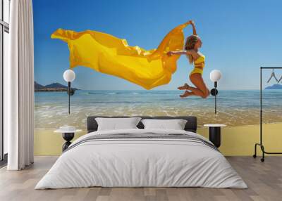 Happy young woman with a yellow light one Cloth jumping at sand beach. Relaxing, fun, and enjoy holiday at tropical paradise beach with blue sky. Girl in summer vacation. Wall mural