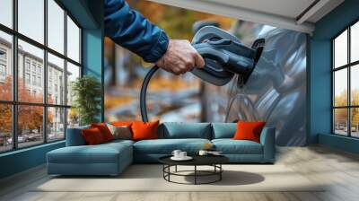 Man holds charging plug for charging car, close up Wall mural