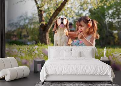 Happy little girl playing with dog in garden. Wall mural