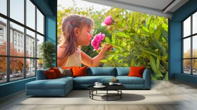 Happy little girl smelling fragrant pink peonies. Wall mural