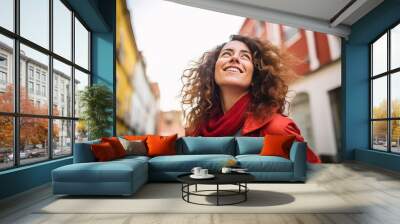 Outdoor portrait of beautiful young woman with curly hair, wearing red coat and scarf Wall mural