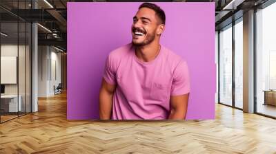 Portrait of a happy young man laughing while standing against purple background Wall mural