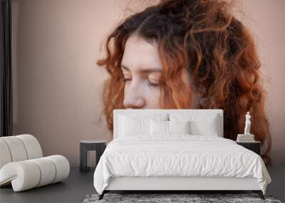 Dreaming young woman with spectacular curly red ginger hair looking at camera posing outdoor in downtown street. Female portrait. Wall mural