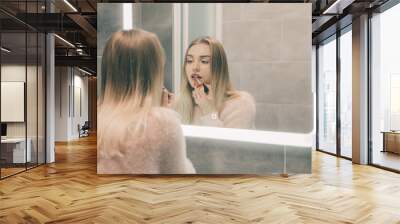 The girl in the bathroom in front of the mirror paints her lips. Wall mural