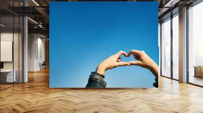 The girl makes a heart with her hands against the background of a rich blue sky Wall mural