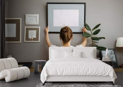 Girl hanging a frame on a gray wall Wall mural