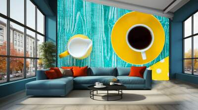 cup of black tea on yellow plate and yellow milk jug..on turquoise colored old wooden table with yellow napkin at polka dots top view Wall mural