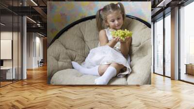 beautiful little girl sitting in the chair with grapes in hand Wall mural