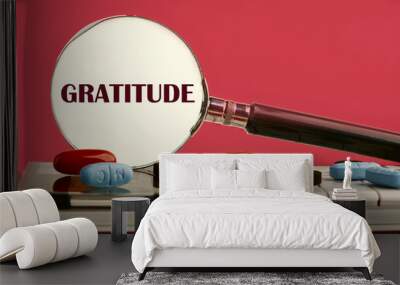 Concept GRATITUDE written through a magnifying glass on a calculator with pills on it on a red background with a white spot from a magnifying glass Wall mural