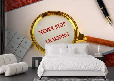 Never stop learning written through a magnifying glass in red letters in a notebook on a blank sheet Wall mural