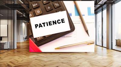 Text PATIENCE on white card with metal pen, calculator and financial charts. Financial concept. Wall mural