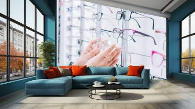 Female customer choosing glasses in an optical store. Girl hands choosing glasses in a store, Female buyer choosing glasses in a store Wall mural