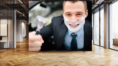 Businessman shaving in car by razor and foam at the wheel. Shaving man in the driver's seat. Hurring. Bluer collar office employee shaveing himself in heavy traffic jam.Beautiful Man in suit Wall mural