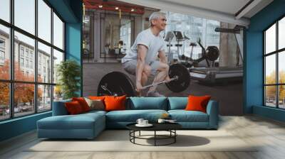 Full length shot of a senior sportsman working out with barbell at gym, copy space. Elderly weightlifter exercising with heavy barbell. Aged fitness man doing deadlift at sport studio Wall mural