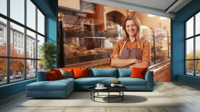 Happy mature small bakery owner smiling proudly at her confectionery store. Cheerful female baker working at her shop Wall mural