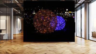 Two glowing balls, one shining with yellow lights, the other blue, against the backdrop of a night city. Wall mural