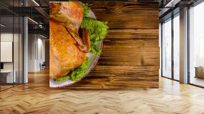 Plate with roasted whole chicken and lettuce leaves on a wooden table. Top view Wall mural