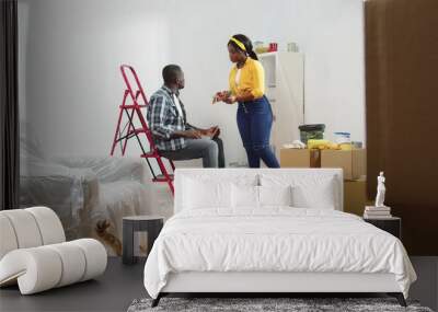 African american couple planning renovation on new home. Portrait of wife and husband sitting on ladder discuss new design living room. Wall mural