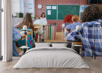 Back view of preteen students sitting on their personal desks at modern classroom. Confident pupils using laptops and tablets while doing exam or solving mathematical equations. Wall mural