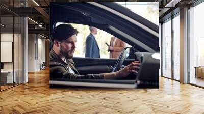 Caucasian buyer take videos on phone sitting inside new purchased automobile in auto salon. Saleswoman manager is typing on tablet standing outside the car and then speaking to another sales manager. Wall mural