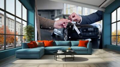 Male hand gives a car keys to male hand in the car dealership close up. Unrecognized auto seller and a man who bought a vehicle shake hands. Wall mural