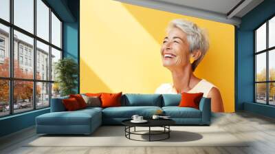 Beautiful senior woman laughing and looking up on yellow background with copy space Wall mural