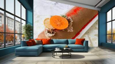 Chocolate yule log christmas cake, also know as Buche de Noel, with tangerine mousse decorated with persimmon, orange chips, star aniseas on wooden background. Festive atmosphere, mood. New Year Wall mural