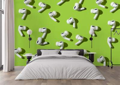 modern wireless headphones for the phone. a lot of plastic air pods on a bright green background. pattern on the theme of communication and music. flat lay, top view. Wall mural