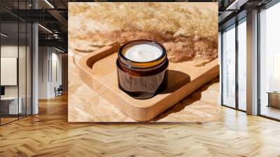 close up of collagen cream in open glass jar and dry flowers reeds on beige background. Set for skin and body care beauty products Wall mural