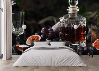 A crystal decanter holding grape fig liqueur two glasses and ripe fruits near it all set on a black background in a close up copy space image Wall mural