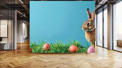 A festive Easter scene with eggs scattered on green grass, a bunny nearby, complemented by a blue backdrop providing ample space for adding text or images. Wall mural