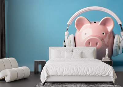 Pink piggy money bank with white wireless headphones over blue background. Copy space image. Place for adding text or design Wall mural