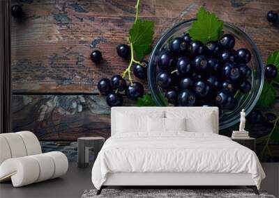 Top down view of a glass dessert bowl containing ripe black currants and leaves on a wooden table providing room for text alongside the image. Copy space image. Place for adding text and design Wall mural