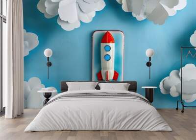 Toy rocket and smartphone placed among white paper clouds on a blue background with copy space image Wall mural