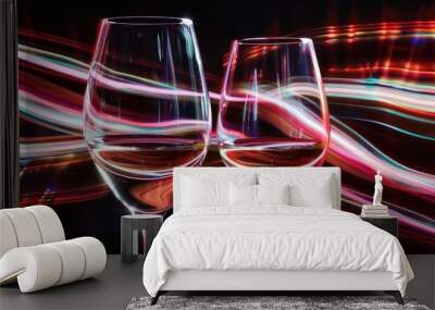 Two wine glasses are isolated against a black background with red white pink and orange neon light creating streaks of illumination behind them This effect showcases light waves color interplay and l Wall mural