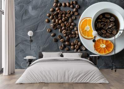 White cup and saucer filled with roasted coffee beans accompanied by two slices of dried orange and a couple of coffee beans set against a gray table background top view. Copy space image Wall mural