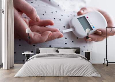 A pregnant woman holds a blood sugar meter in her hand and brings a test strip to a drop of blood on her finger Wall mural