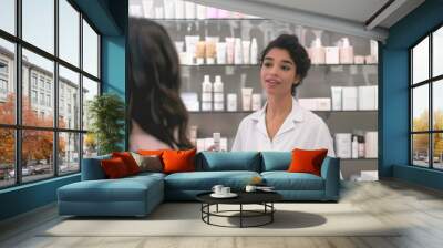 Cosmetics salesperson stands in front of shelves filled with various beauty products, holding and promoting cosmetics to customer. Personalized service and product recommendations in retail setting. Wall mural