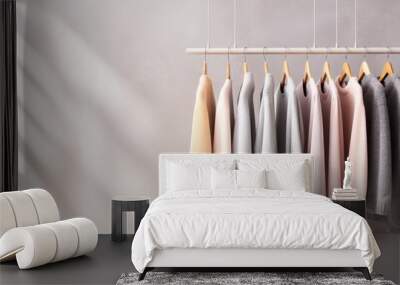 Pastel-colored sweaters hanging on hangers. Minimalist apparel display, white wall background Wall mural