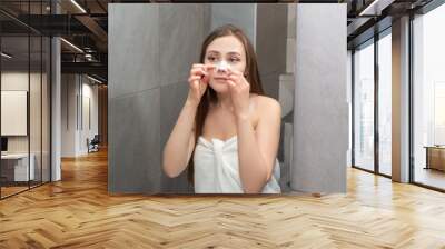 Young woman recovers a strip on her nose for deep cleansing of the skin on her nose. Concept of facial skin care in the bathroom every morning. Wall mural