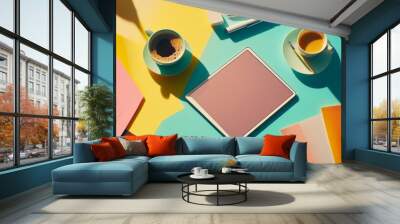 A lively workspace features two cups of coffee, colorful sheets of paper, and a tablet in a playful arrangement, bathed in natural light and vibrant shadows Wall mural