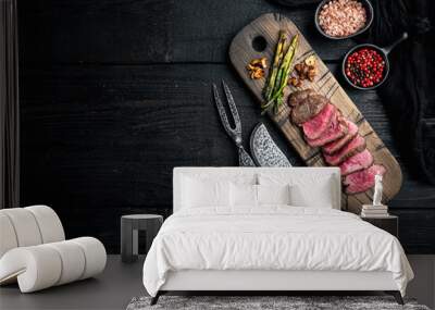 Juicy steak medium rare beef Filet Mignon or Eye Fillet, with onion and asparagus, on wooden serving board, with meat knife and fork, on black wooden table background, top view flat lay Wall mural