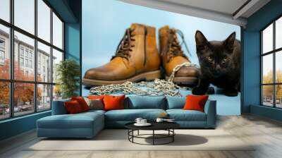 A black cat sits to the right of a pair of new boots against a blue background. Fashionable concept. Wall mural