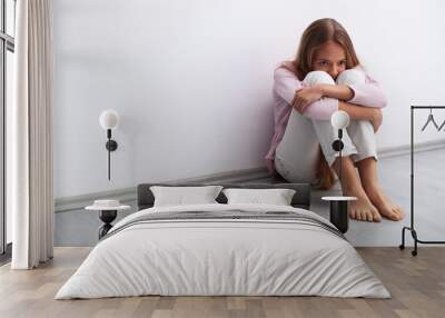 Young worried or sad girl sitting on the floor by the wall Wall mural