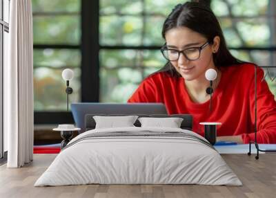 Happy woman studying online at home, smiling while using laptop and notebook at her desk Wall mural