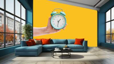 Clock. Alarm clock in a female hand on a yellow background. Wall mural