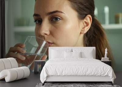 Thirsty young woman drinking fresh water from glass. Home office kitchen interior. Headshot portrait. Dehydration prevention, normal bowel function and balance of body maintenance concept Wall mural