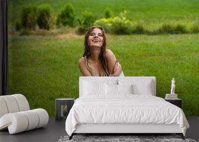 Attractive girl enjoys life, plays, wallows on a green fresh lawn in the rain. Wet hair and wet dress from watering the lawn Wall mural