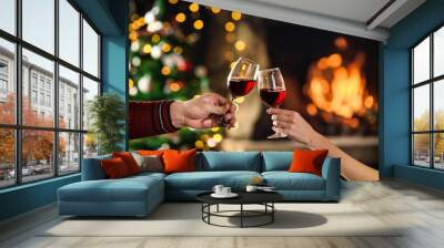 Celebrate christmas with red wine in glasses. Couple clink glasses near fireplace. Hands closeup Wall mural